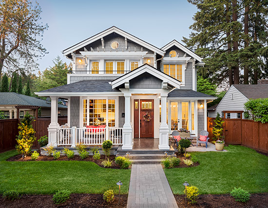 A gray and white home is lit with lights as the sun sets.