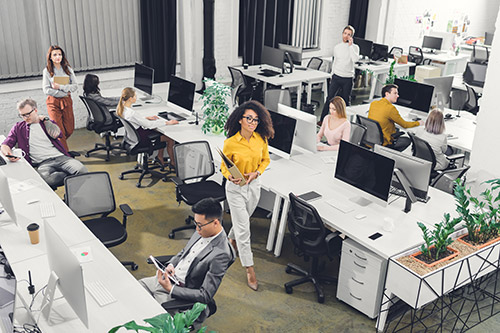 A photo of a busy office with people using lots of computers and other electronics.