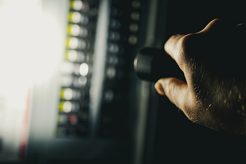 An image of someone checking a breaker box using a flashlight in the dark.