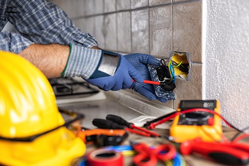 An electrician wearing blue gloves works on an outlet in a customer's home